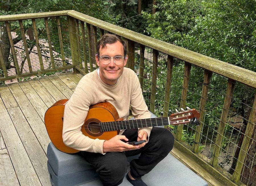 Jonatan Littke playing guitar on a deck in the redwoods